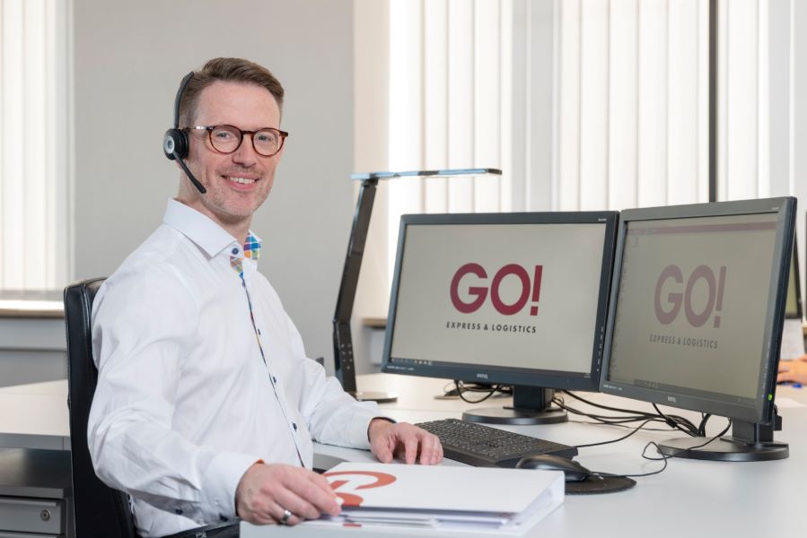 Mitarbeiter (m/w/d) GO! Express & Logistics GmbH Ein kaufmännischer Mitarbeiter (m/w/d) von GO! Express & Logistics GmbH sitzt an seinem Schreibtisch. Vor ihm stehen zwei Monitore, seine Tastatur und seine PC-Maus sind vor ihm. Er will gerade einen Ordner mit Unterlagen öffnen um etwas nachzulesen