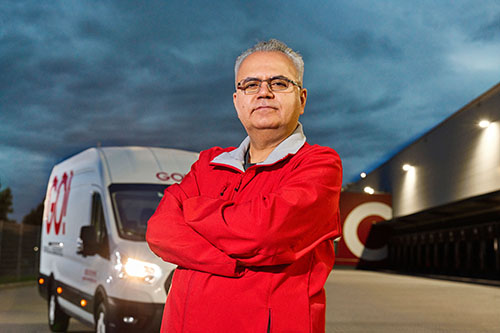 Ein Mitarbeiter (m/w/d) von GO! Express & Logistics steht vor einem unserer Transporter. Er trägt eine rote Jacke.
