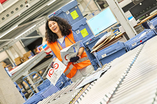 Team von Mitarbeitern aus dem Büro, Lager und Kuriere in einem Sortierzentrum. Alle tragen passende Arbeitskleidung und schauen entschlossen in die Kamera.
