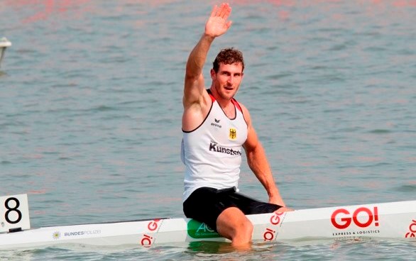 Sebastian Brendel winkt zur Kamera Sebastian Brendel sitz auf seinem Kanu, mit GO! Logo, im Wasser und winkt zur Kamera