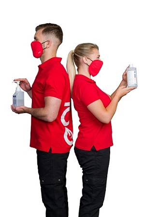 Zwei GO! Mitarbeiter in roten GO! T-Shirts stehen Rücken an Rücken. Beide Tragen rote OP-Masken und halten je eine Flasche mit Desinfektionsmitteln in den Händen