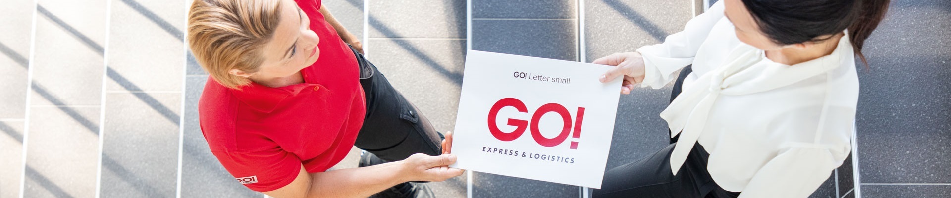 GO! Kurierin übergibt Letter an eine Geschäftsfrau auf einer Treppe
