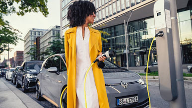 Eine Frau steht vor einem Elektroauto und hält das Ladekabel einer Ladesäule