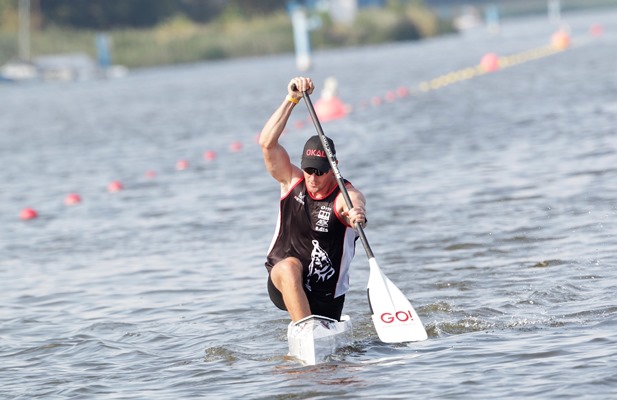 Sebastian Brendel paddelt, im Wettrennen, auf seinem Kanu im Wasser. Auf dem Paddel ist das GO! Logo zu sehen.