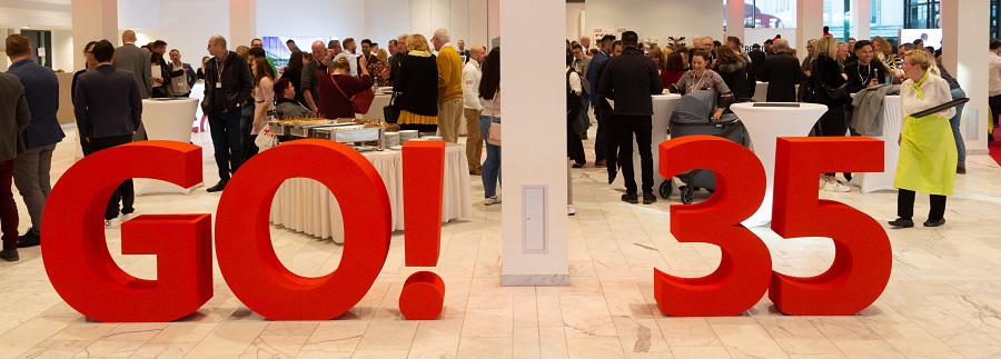 GO! 35 Jahre GO! und die Zahl 35 als Statuen in einem Saal. Im Hintergrund Feiern Mitarbeiter und Gäste von GO! das fünfunddreißigste Geburtstag von GO!