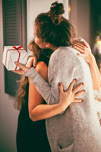 Zuhause umarmen sich zwei Frauen, eine hält ein kleines Geschenkpaket in einer Hand