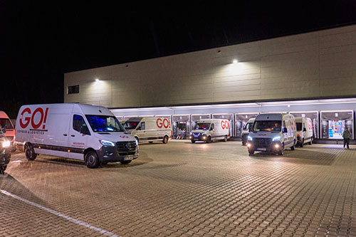 Kurierfahrzeuge von GO! Express & Logistics stehen vor einer unserer Stationen. Einige stehen an Toren und werden gerade be- oder entladen