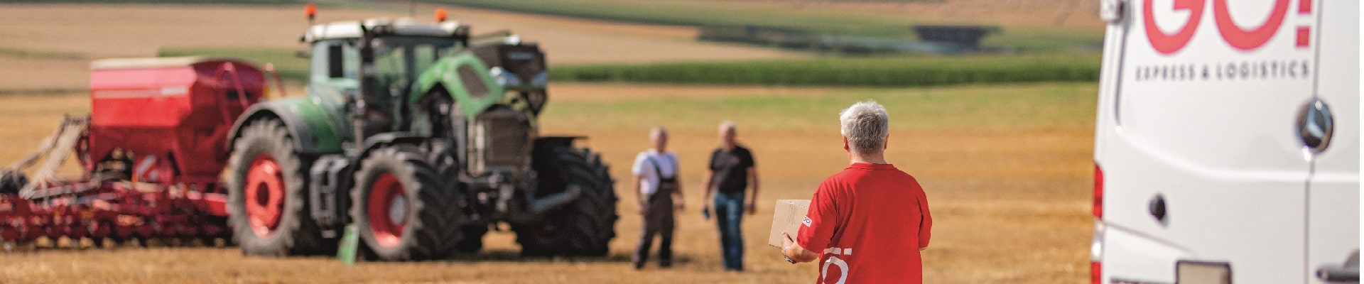 GO! Kurier liefert Ersatzteil an zwei Landwirte, welche auf einem Feld neben einem beschädigten Traktor stehen