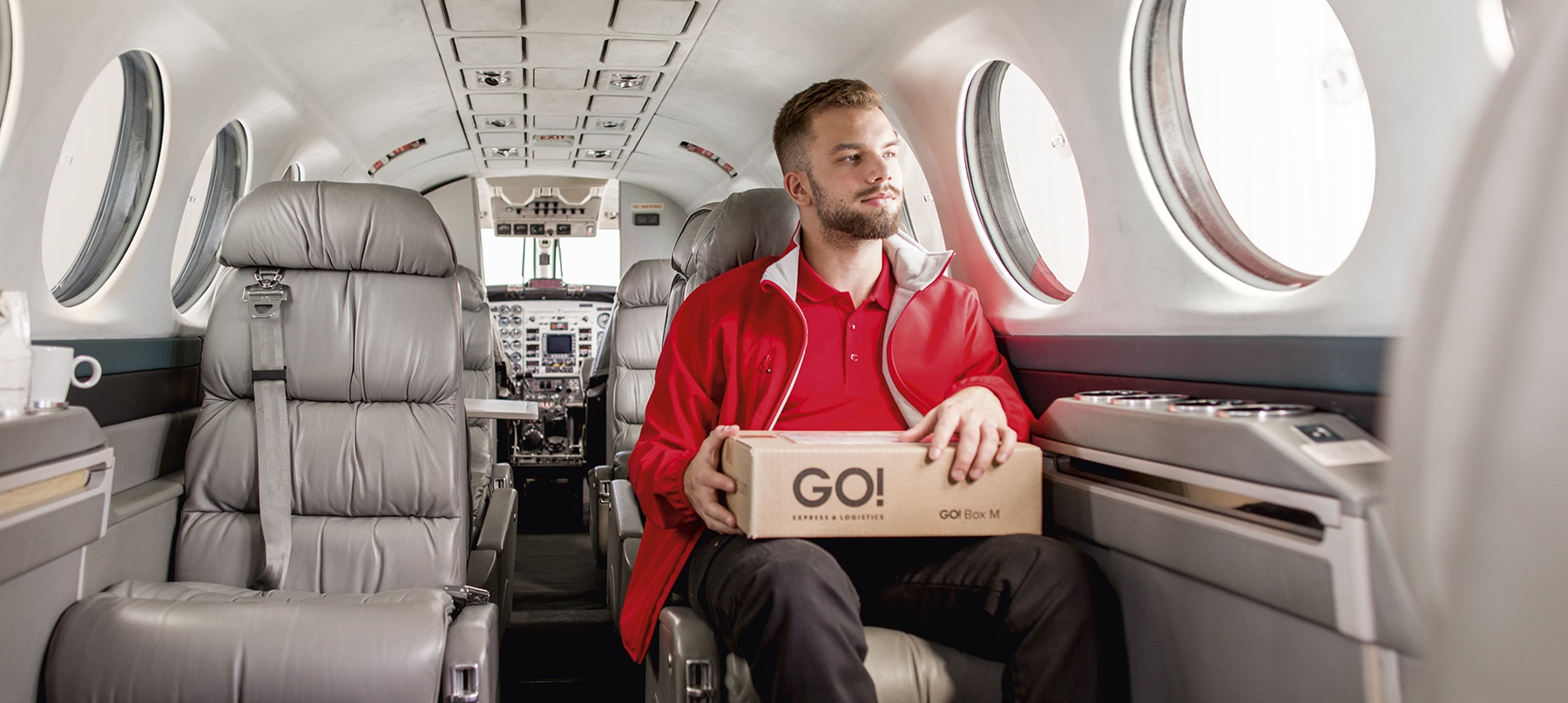 GO! On-Board-Courier sitzt mit Paket auf dem Schoss in einem Businessjet